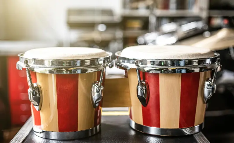 Paire de bongos en bois rayé rouge et naturel, posée devant une batterie