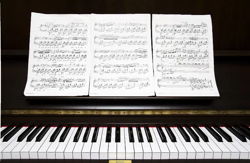 Trois feuilles de partition ouvertes sur le pupitre d'un piano droit, au-dessus du clavier