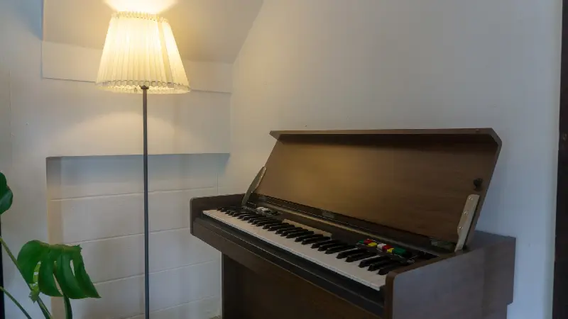 Orgue électrique ancien au couvercle ouvert, à côté d'un lampadaire allumé dans un coin de pièce