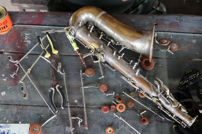 Vieux saxophone terni en cours de démontage sur un établi, clés, tampons et pinces éparpillés autour