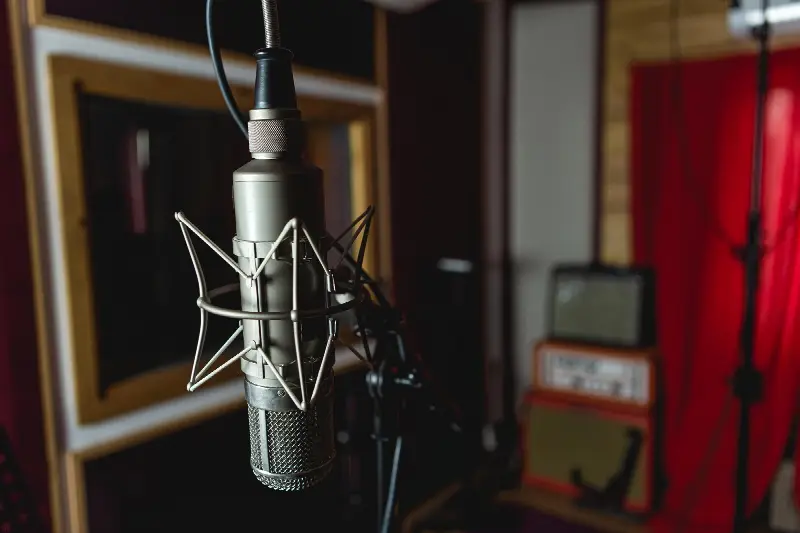 Grand micro à lampe ancien dans sa suspension élastique, dans une cabine de studio, amplis de guitare au fond