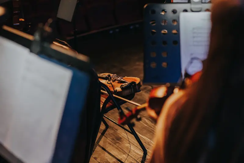 Violon posé sur une chaise entre des pupitres, une violoniste qui joue au premier plan pendant une répétition