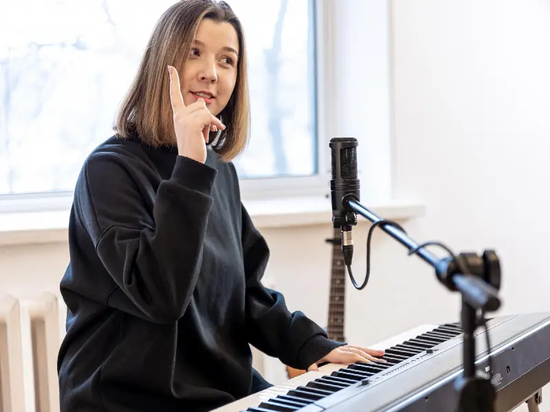 Chanteuse assise à un piano numérique devant un micro, l'index levé, pendant une séance de chant