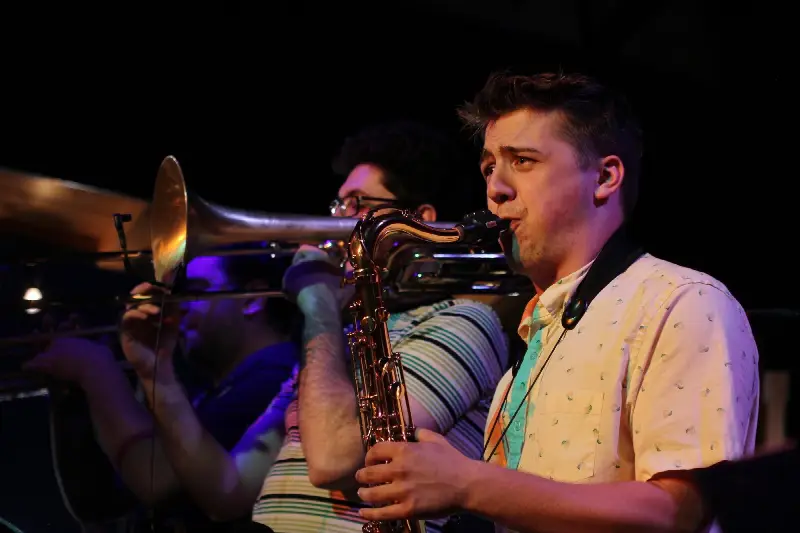 Un saxophoniste ténor et un tromboniste jouent côte à côte sur une scène sombre